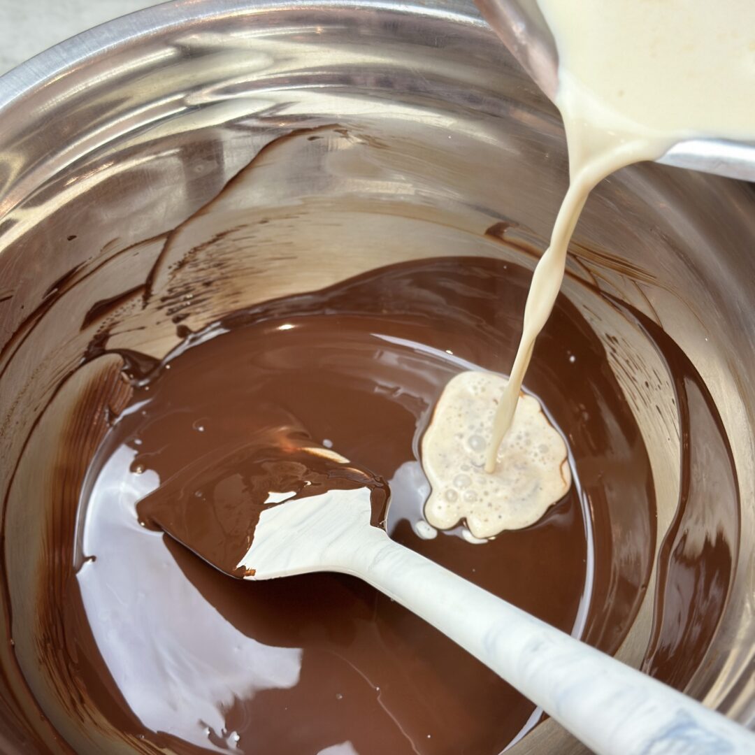 Hot whipping cream being poured over melted dark chocolate to make a dark chocolate whipped ganache