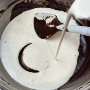 Cold whipping cream being added to a dark chocolate ganache to make it a dark chocolate whipped ganache